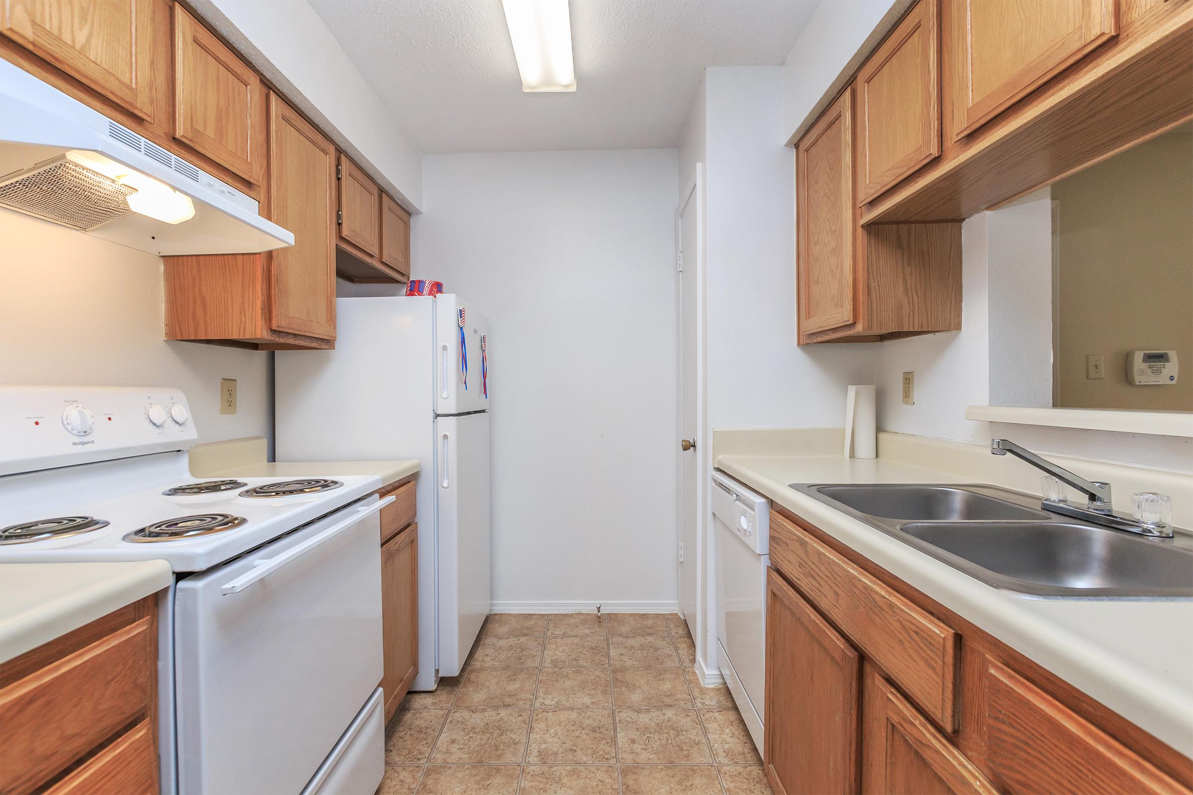 Kitchen with wood cabinets, white appliances, and tile flooring.