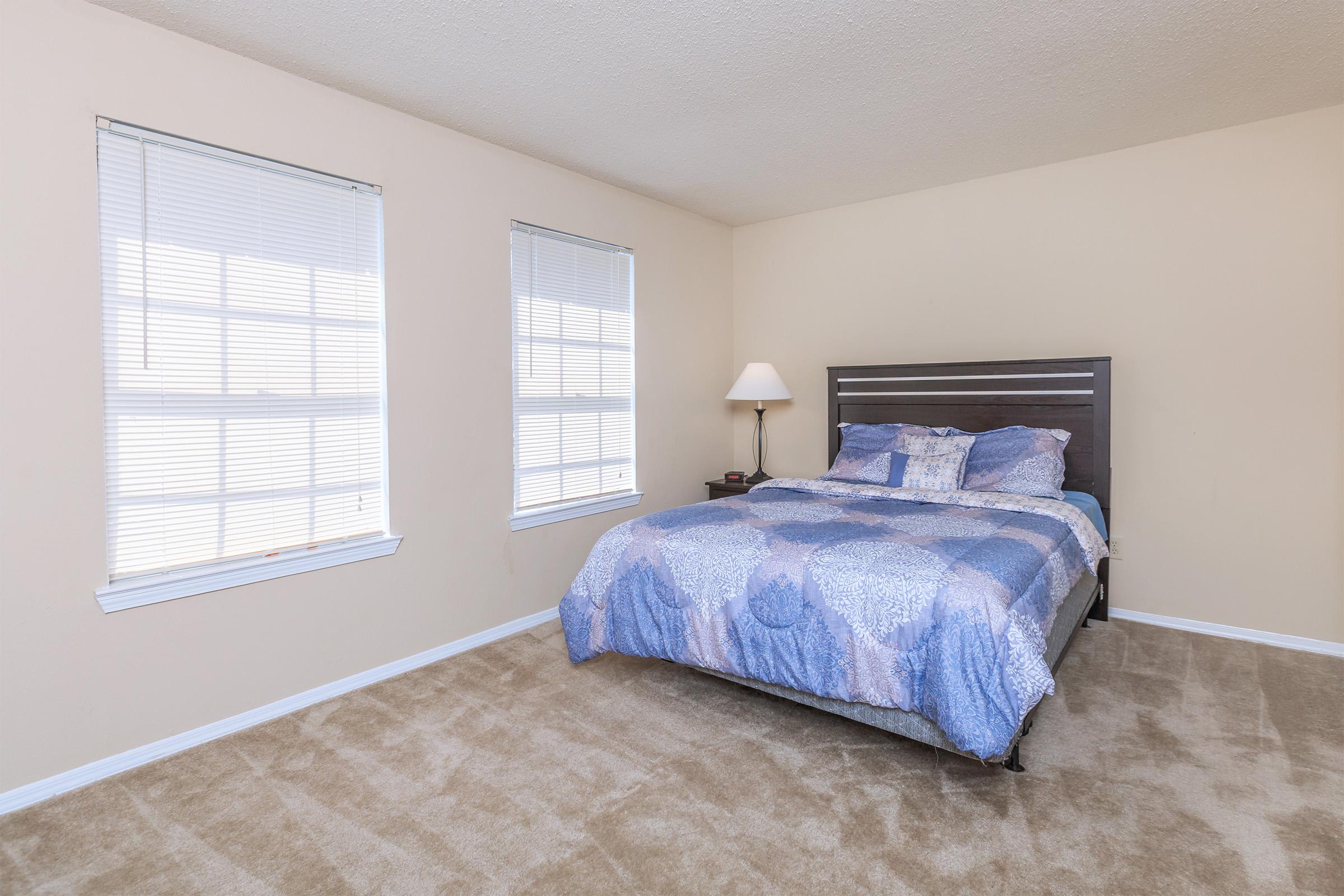 Bedroom with blue bedding and two windows.