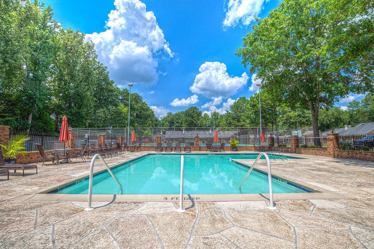 Outdoor pool with lounge chairs and sunny sky.
