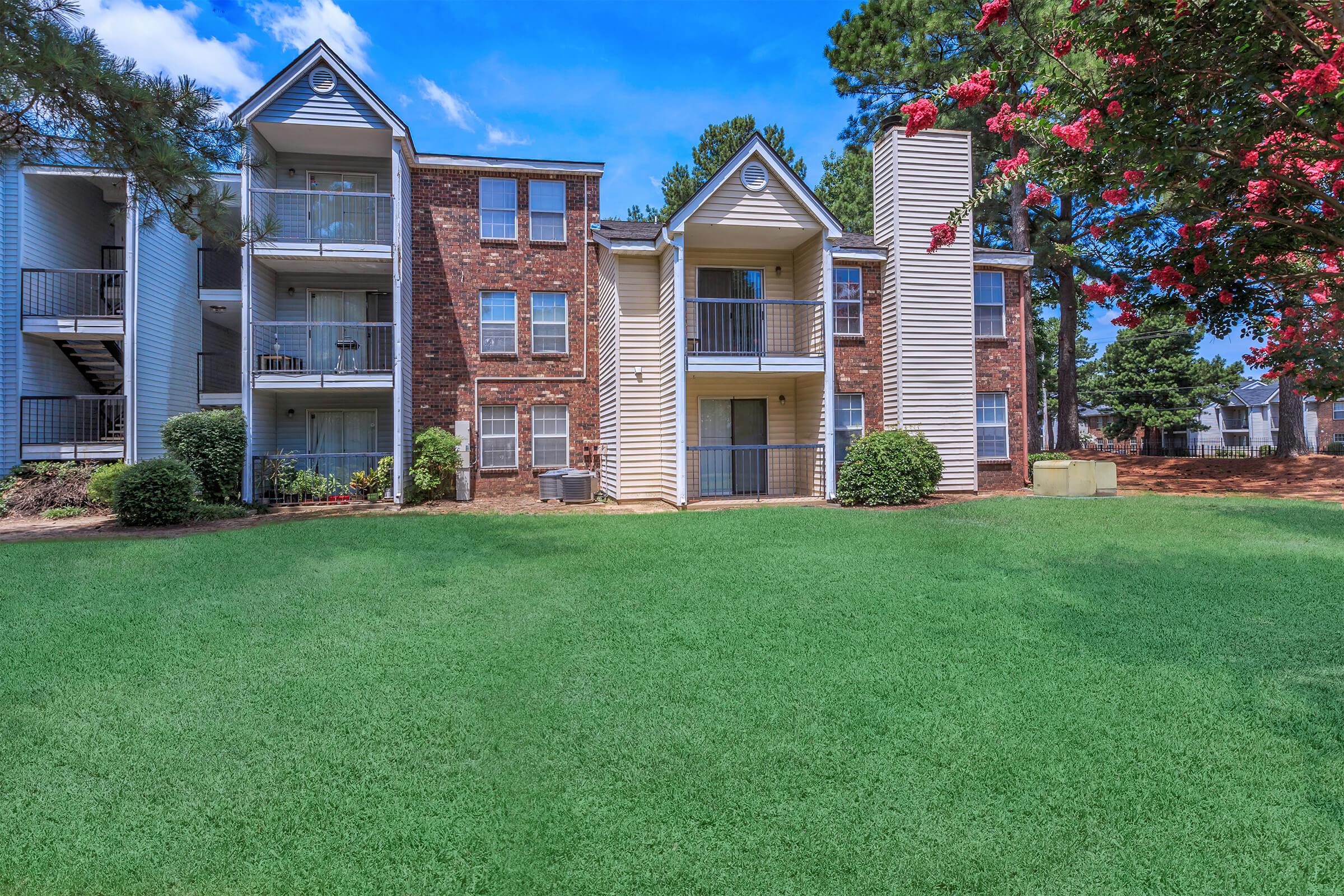 Apartment complex with brick and siding exteriors surrounded by greenery.