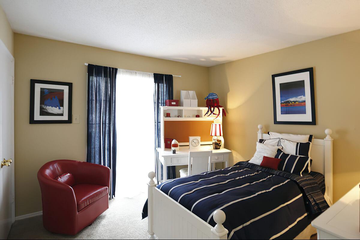 Bedroom with a bed, chair, and bright natural lighting.