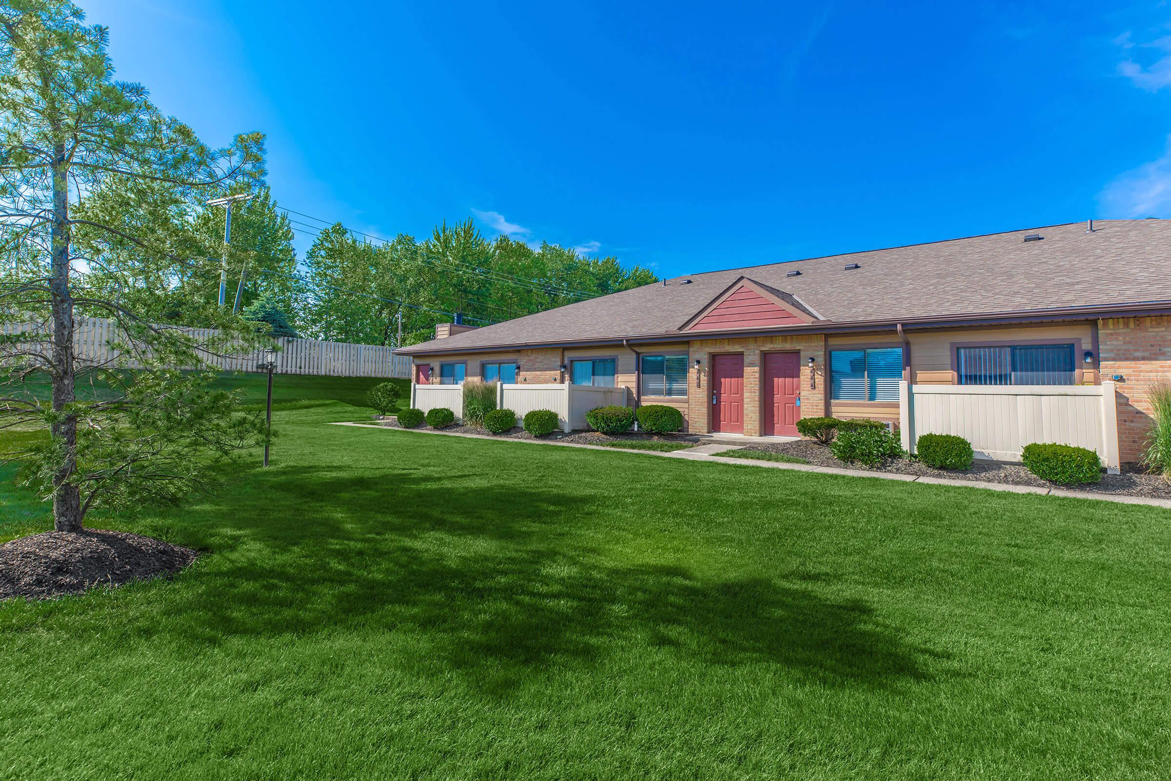 Grass lawn in front of apartment units with trees and greenery.