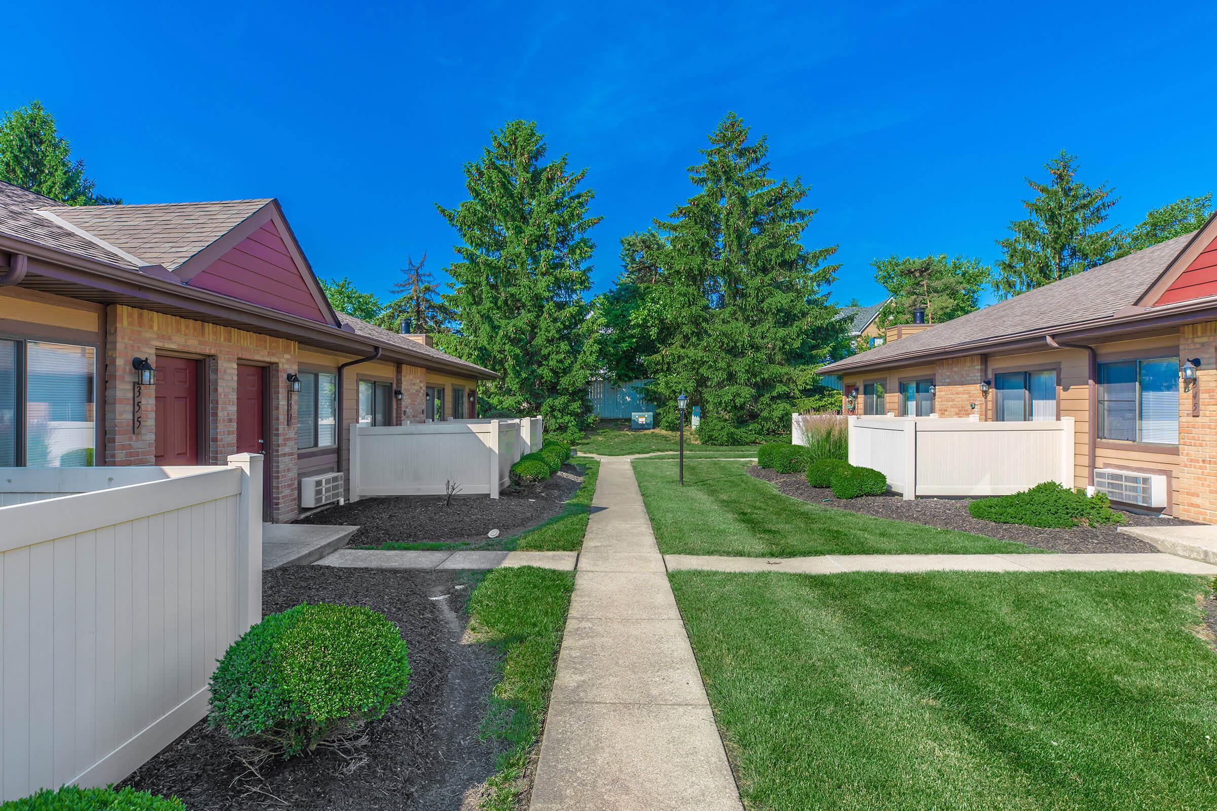 Walkway leading to apartment units with trees and grass.