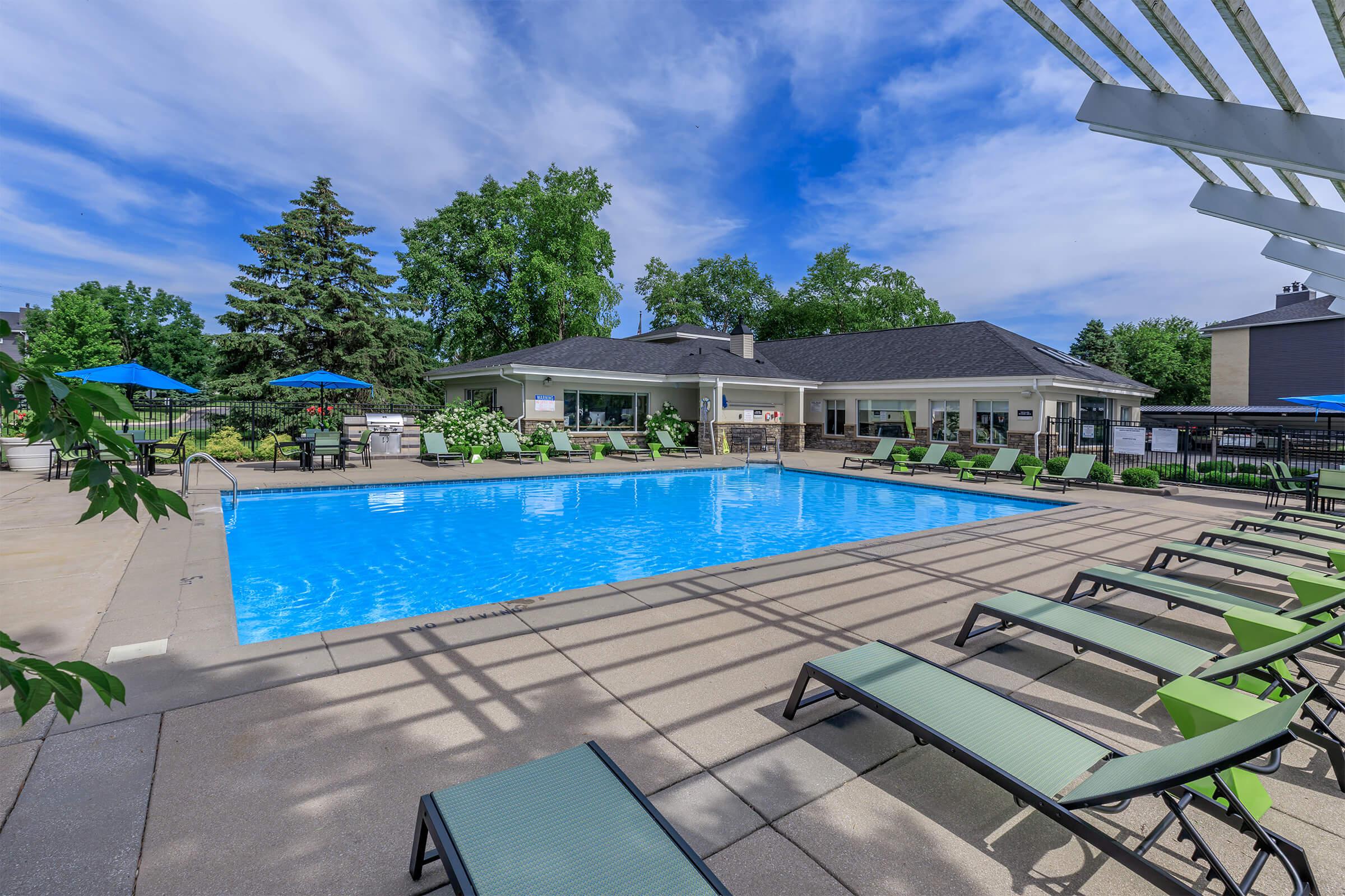 Exterior view of the pool with green trees and lounge chairs.