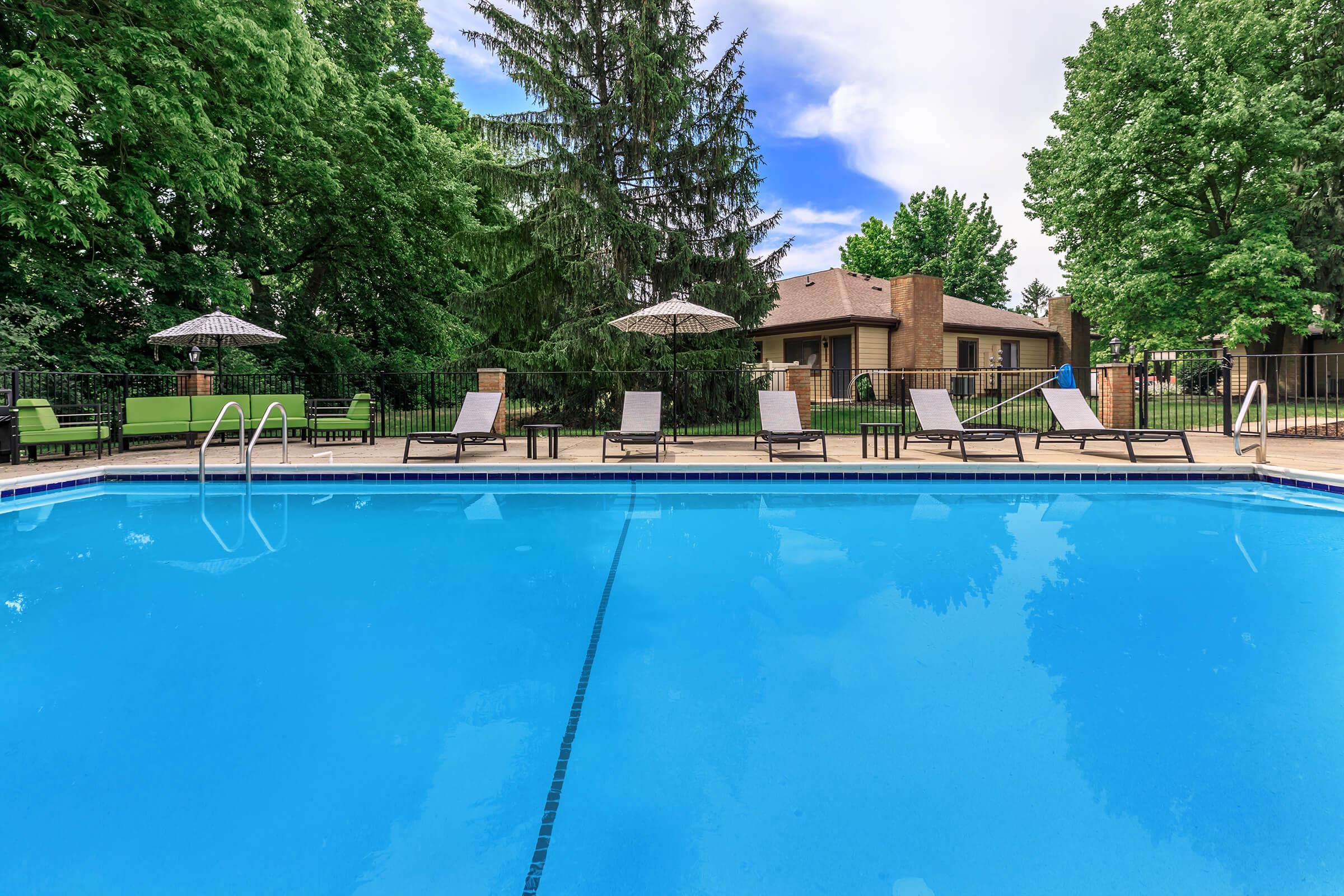 Outdoor swimming pool with lounge chairs and trees.