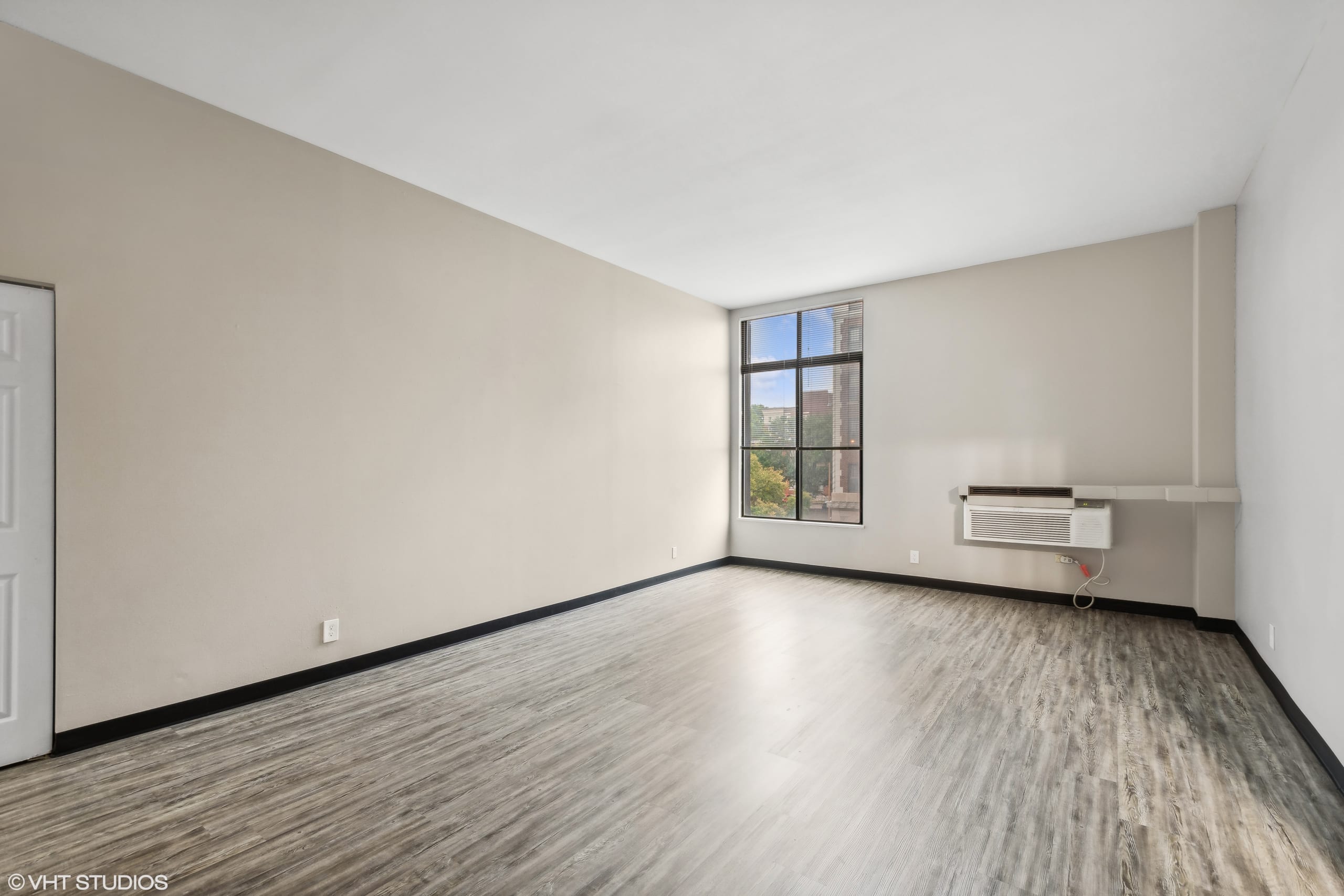 Spacious living room with large window and wood flooring.